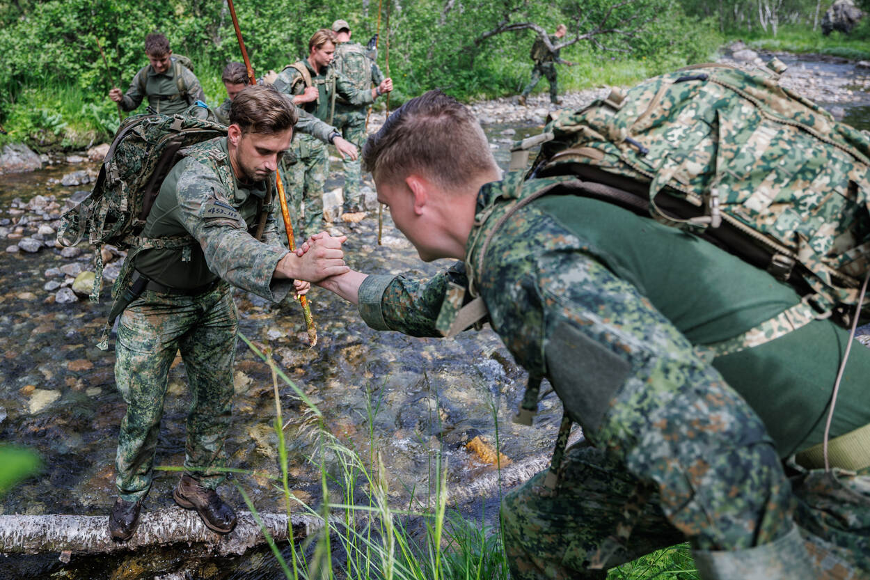 Militairen helpen elkaar een riviertje over te steken.