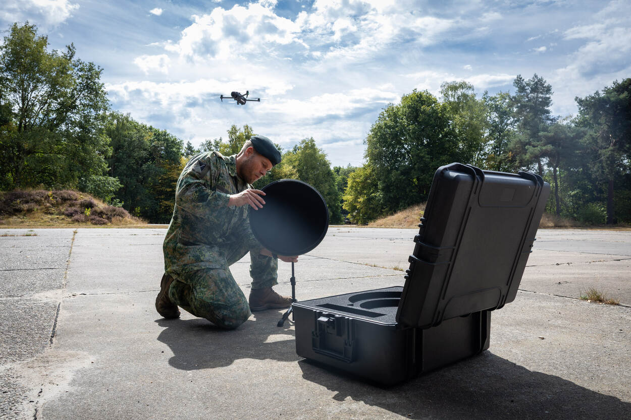 Een militair bouwt een groen gesproten BeephoniX M2 op. Boven zijn hoofd vliegt een drone.