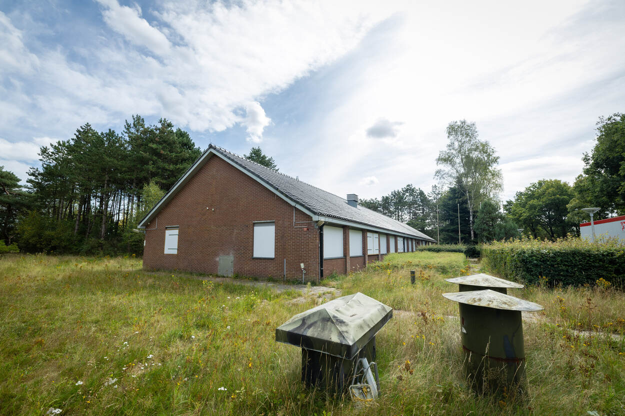 Bakstenen gebouw met puntdak en dichtgetimmerde ramen met gras eromheen.