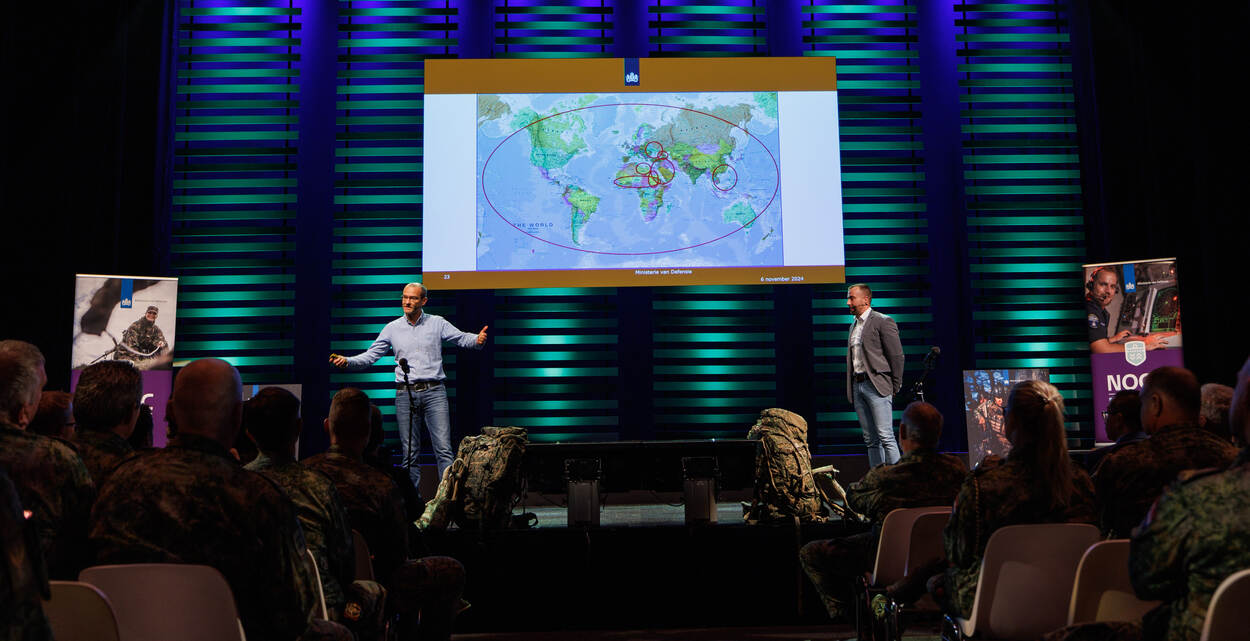 Twee mannen pratend op het podium met een wereldkaart tussen hen in.