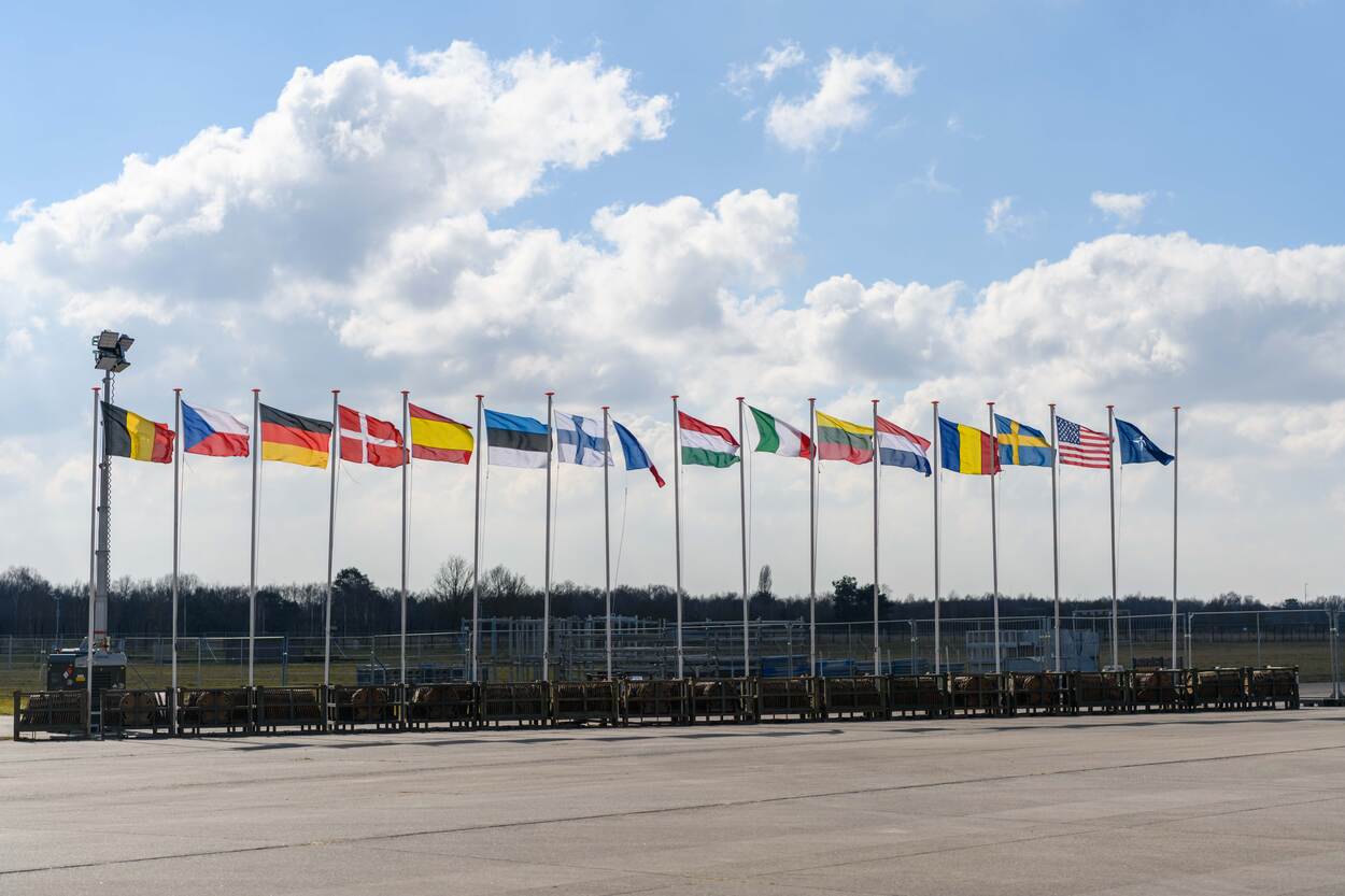 Zestien vlaggen wapperen naast elkaar. Aan het einde de NAVO-vlag.