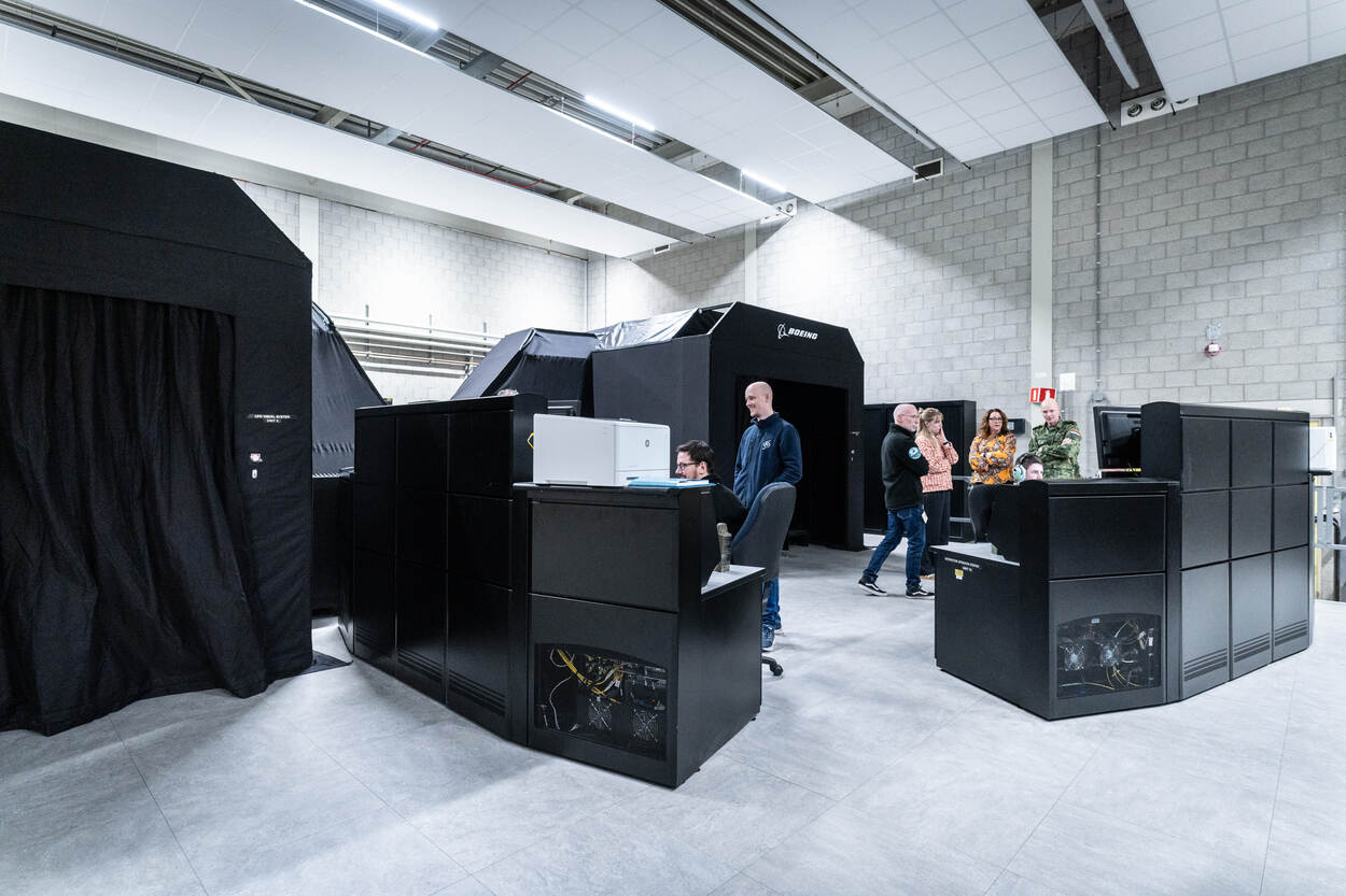 Een open ruimte met daarin zwarte hokjes, waarin de simulators van de Apache Echo staan. Daartussen een rij met beeldschermen waarop personen meekijken.