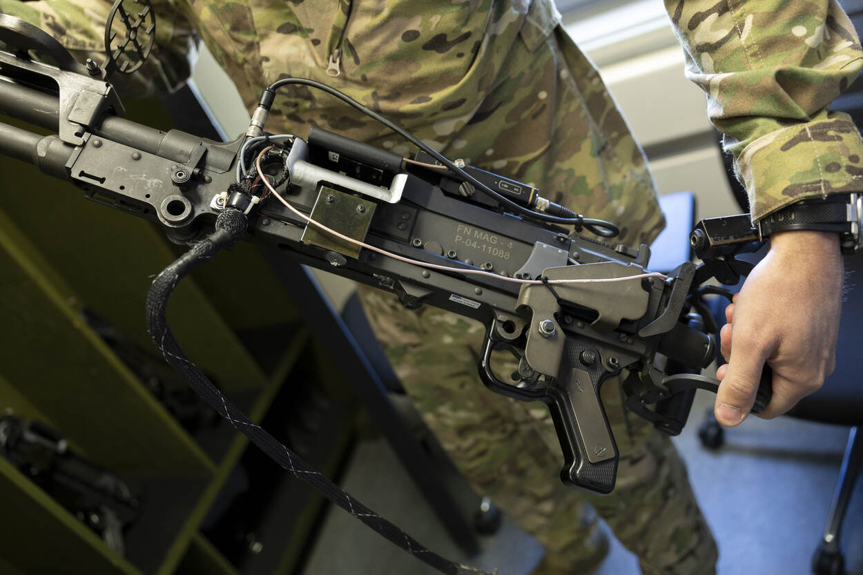 Clarence houdt een boordwapen in zijn handen dat in de simulator geplaatst kan worden.