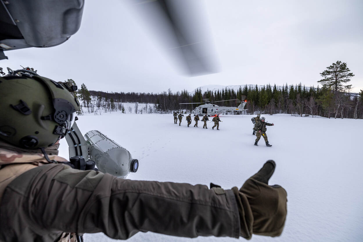 Mariniers lopen in de sneeuw. De voorste steekt zijn duim op naar een bemanningslid van de NH90 die hetzelfde doet.