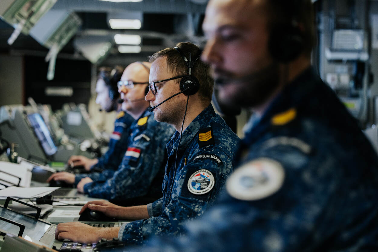 Vier marinemannen achter elkaar gezien, kijken naar hun computerschermen.