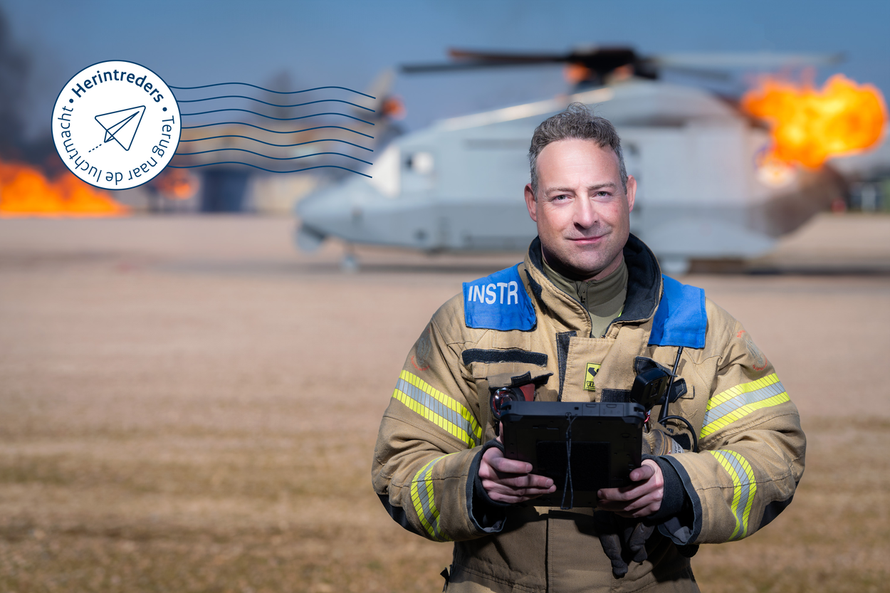 Sergeant-majoor Martijn Versteeg poserend voor een brandende helikopter op het brandweeroefenterrein.