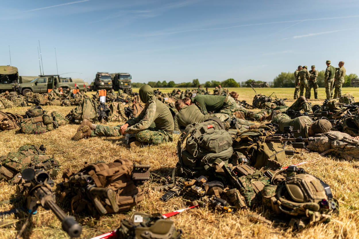 Militairen naast hun persoonlijke uitrusting ontspannen in het gras.
