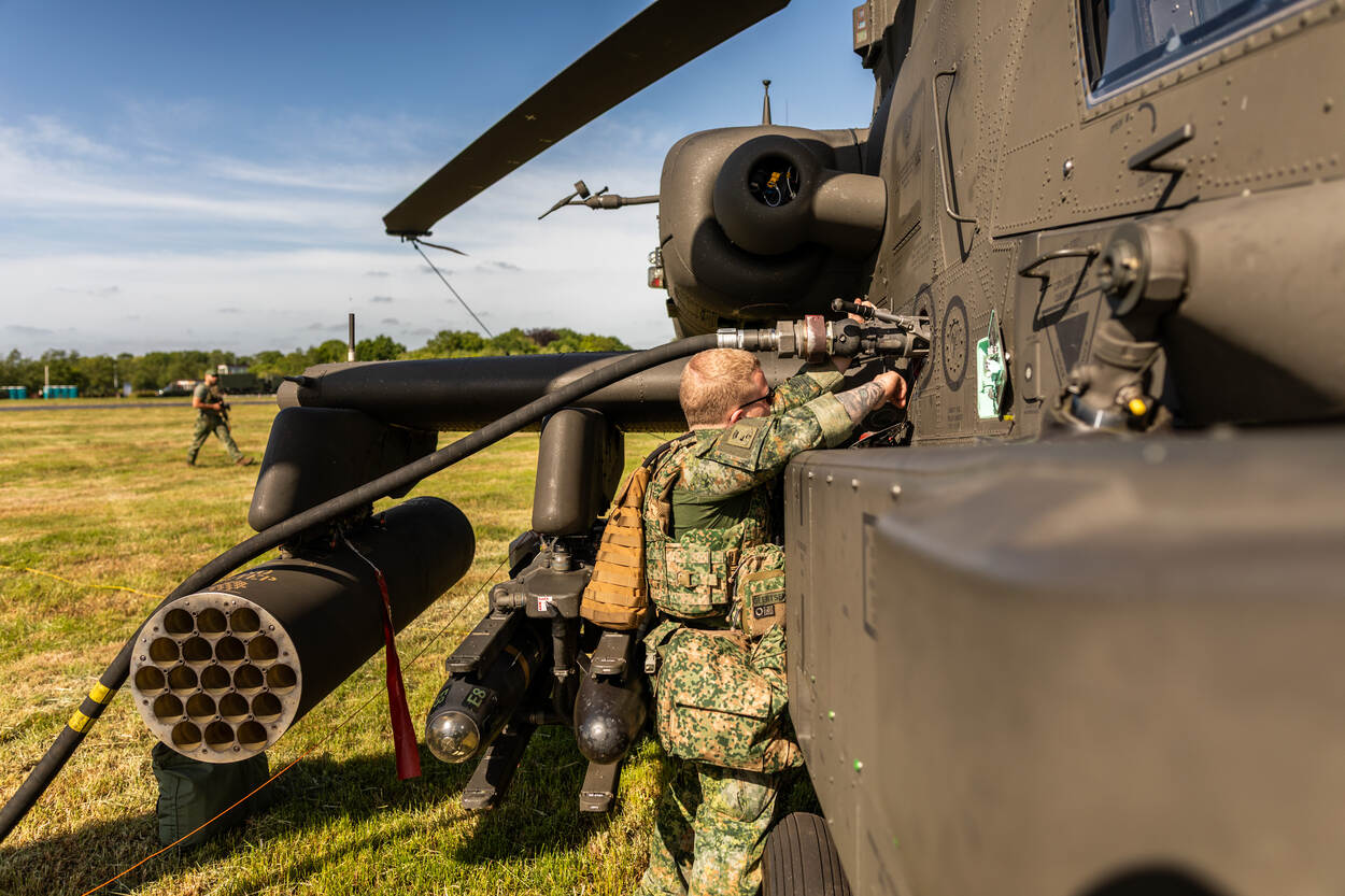 Militair tankt helikopter bij op een grasveld.