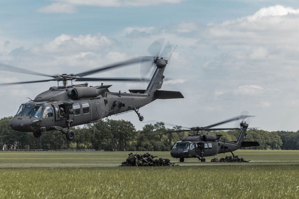 Twee opstijgende Black Hawks, onder hen twee groepen militairen in een huddle.