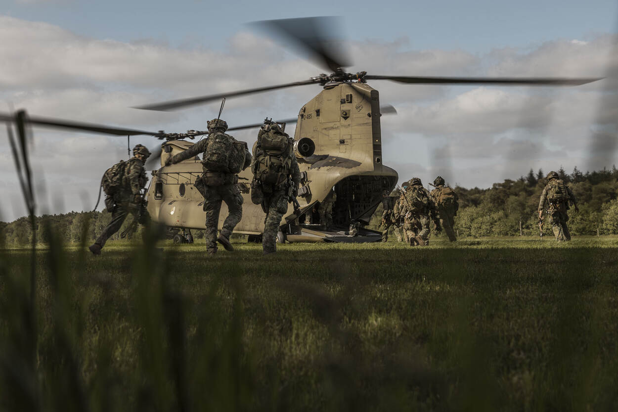 Militairen in het veld lopen naar een openstaande Chinook met draaiende rotors.