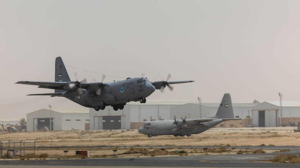 En Jordaanse C-130 stijgt op terwijl een C-130 van de Verenigde Arabische Emiraten naar de startbaan taxiet.