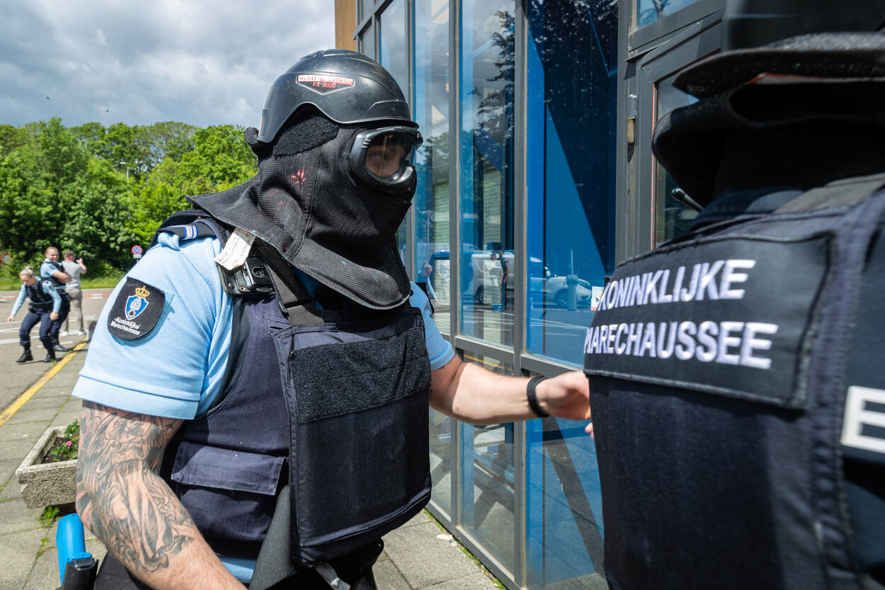 Een marechaussee met masker en vest betreedt een gebouw op de luchthaven.