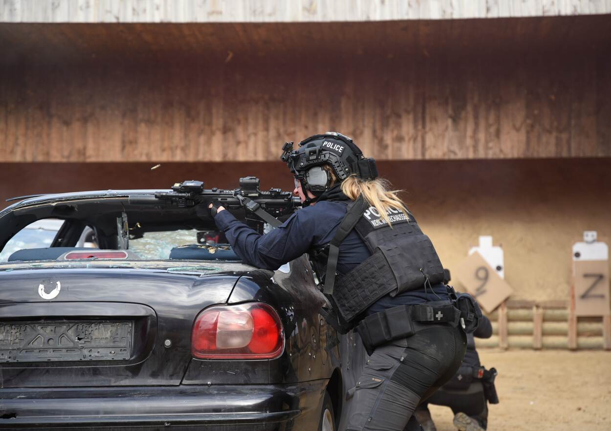 Sophie en Sara schieten tijdens de opleiding, schuilend achter een auto.