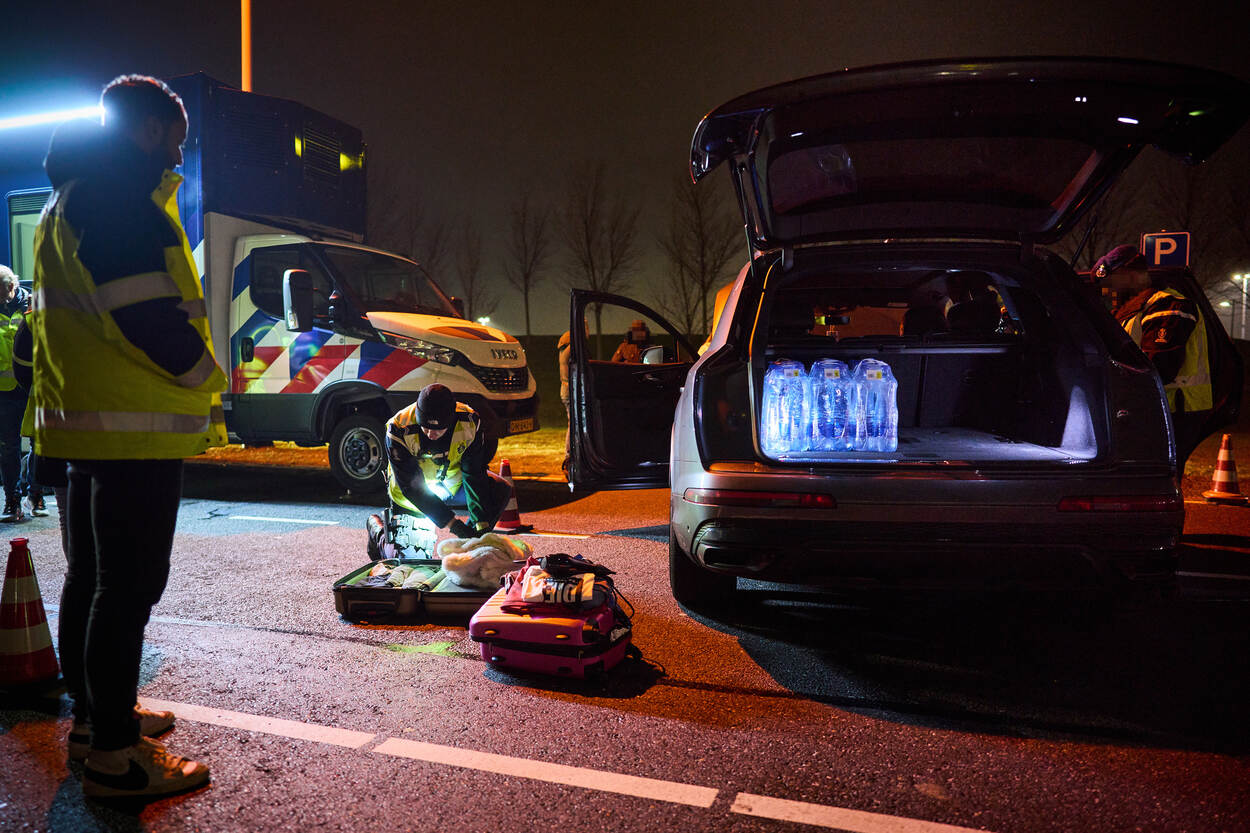 Marechaussee doorzoekt koffers naast een auto.
