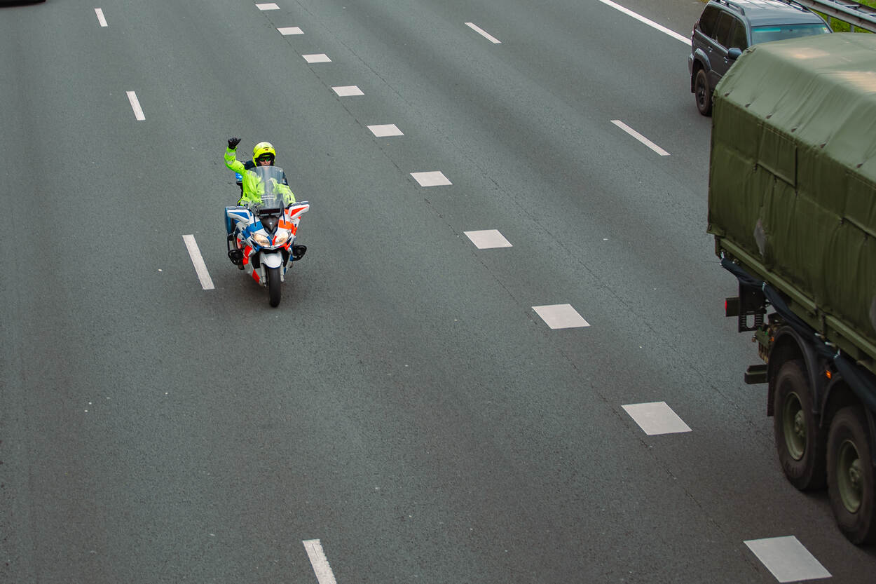 Een motorrijder begeleidt een militaire colonne op de snelweg.