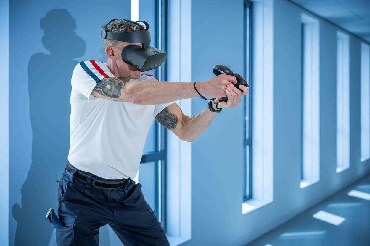 Adjudant Marcel in schiethouding. Hij showt de VR-bril en controllers.