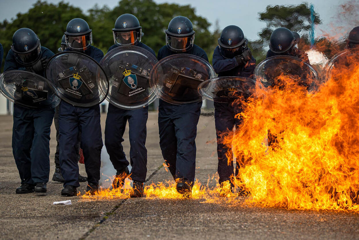 Bijstandseenheid van de Marechaussee oefent met vuur op de voorgrond.