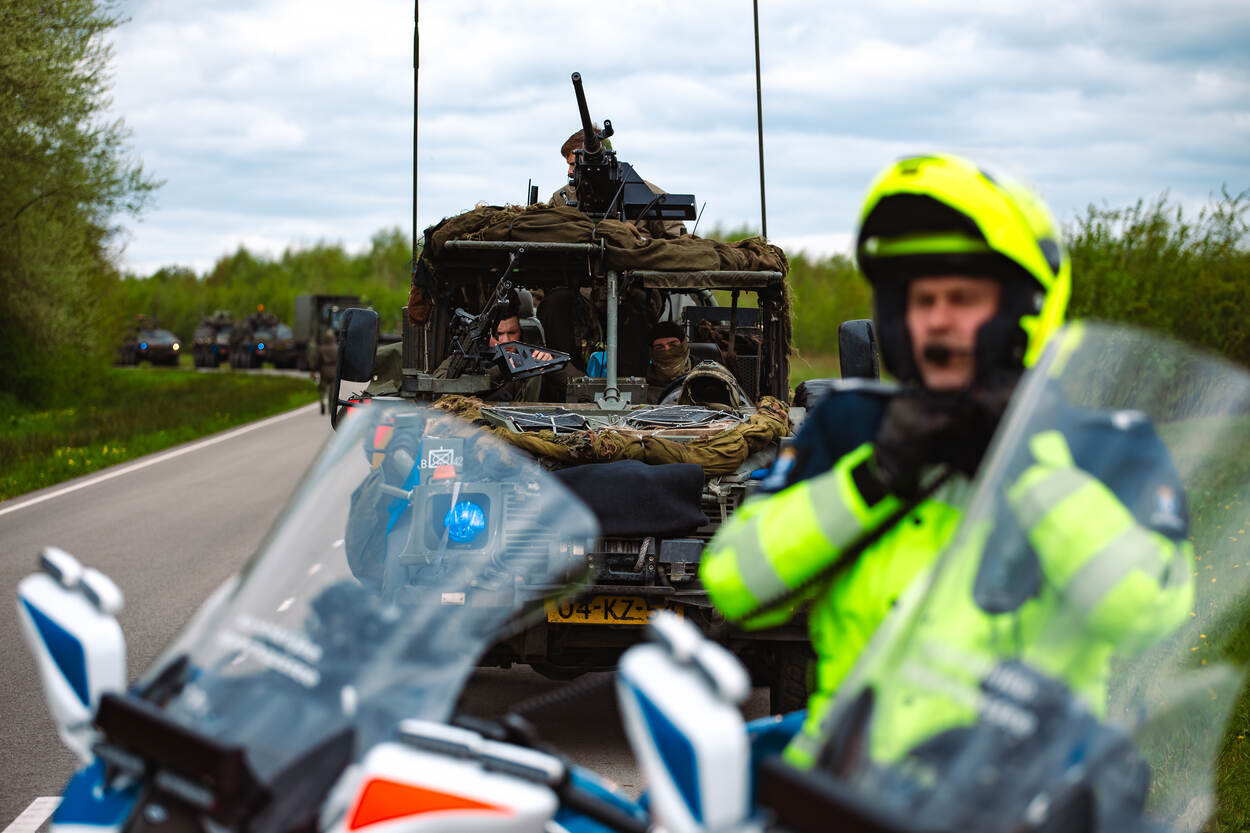 Motorrijder van de Marechaussee, op de achtergrond militaire voertuigen