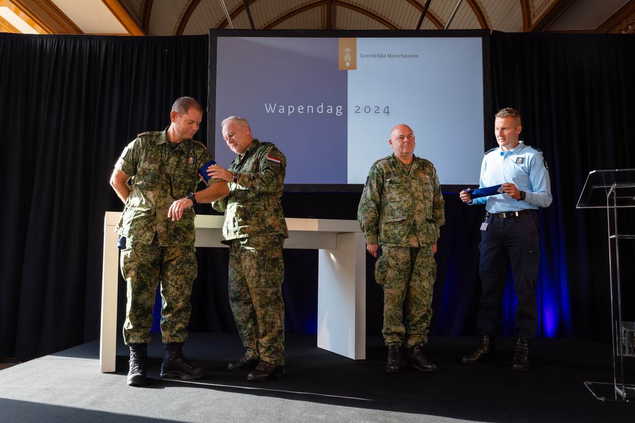 De CDS die een armband over de arm van commandant Den Heijer schuift.