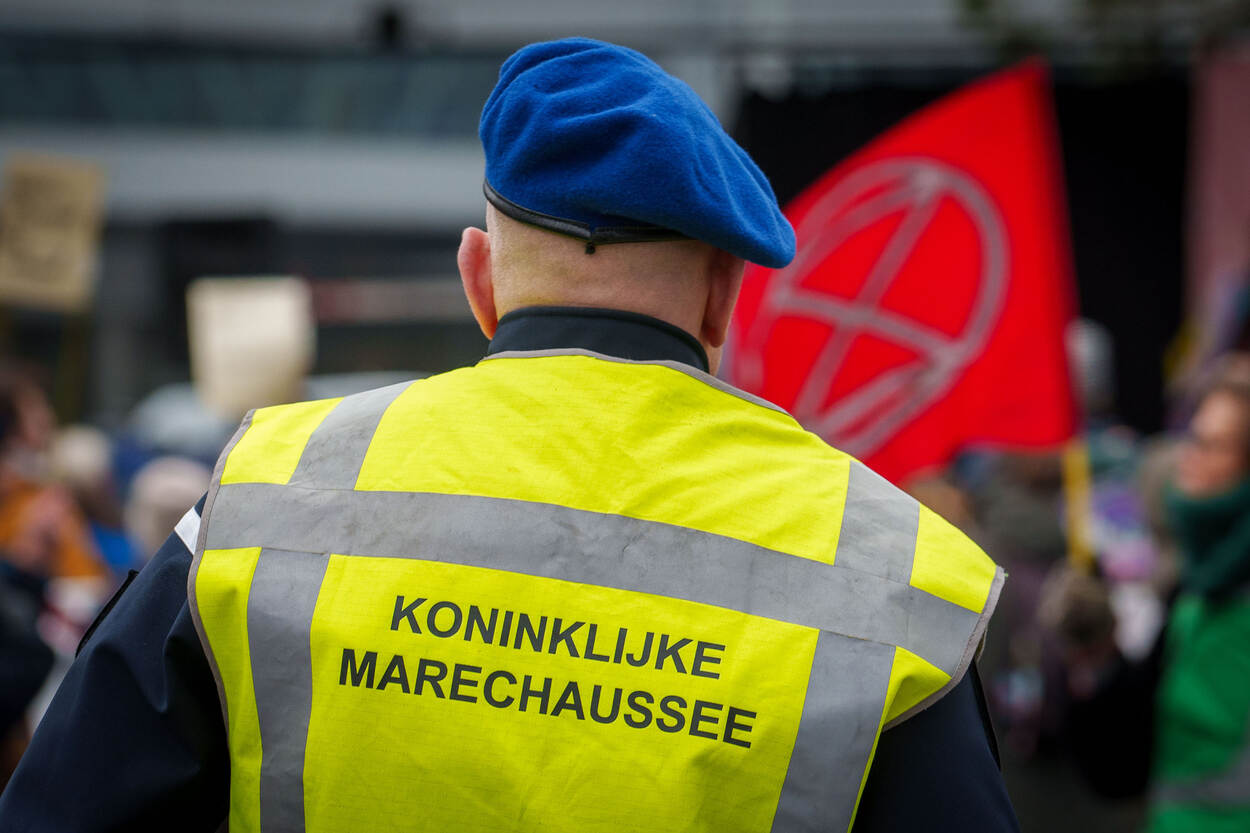 Een marechaussee op de rug gezien, houdt de demonstranten in de gaten.