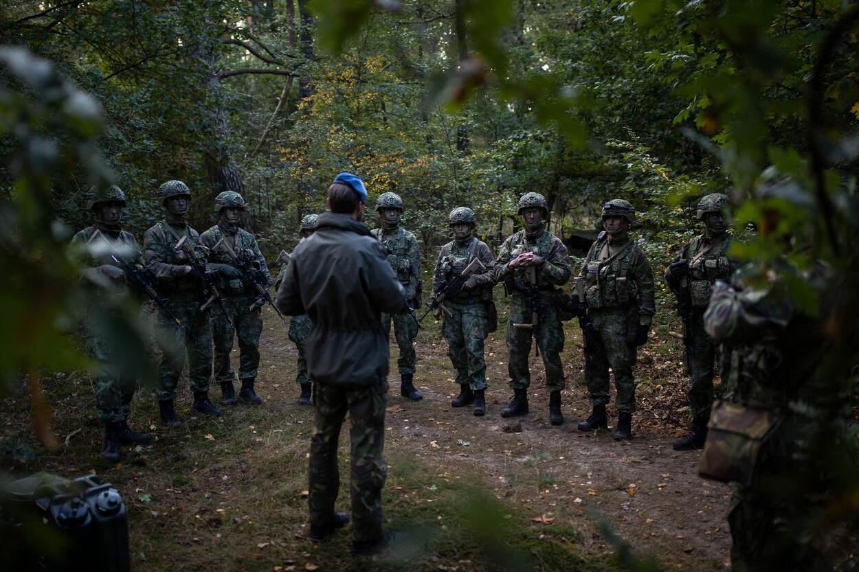 Marechaussees in opleiding krijgen instructie in het bos. Ze dragen camouflagekleding.