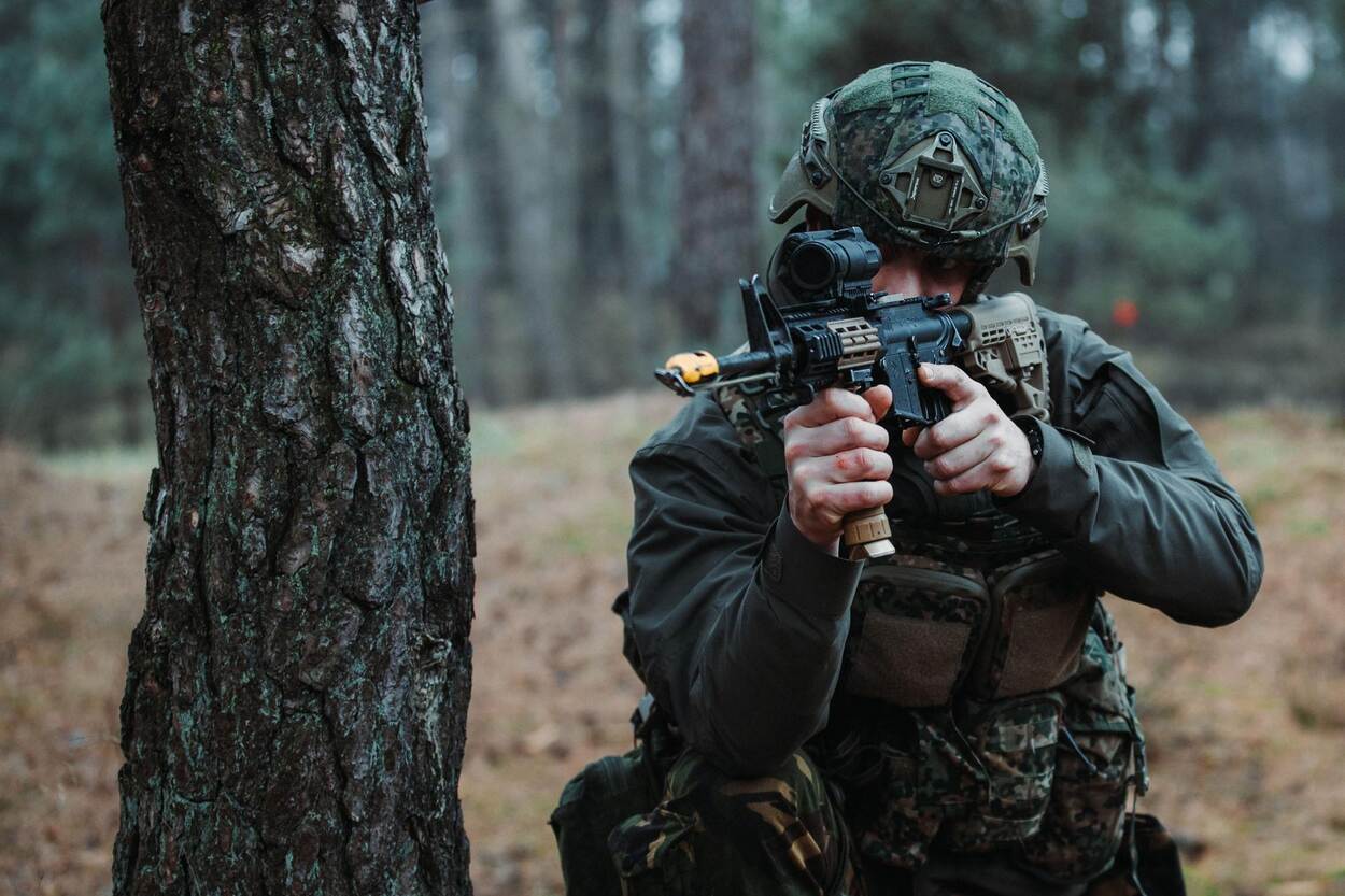 Een Marechausseereservist in camouflagepak en met helm op richt zijn geweer tijdens een oefening.