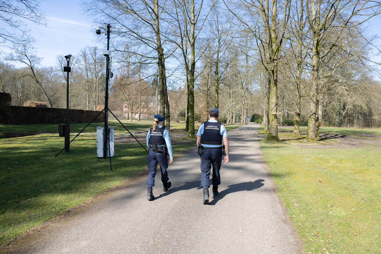 2 marechaussees lopen door een park langs een camera met een radar eronder.