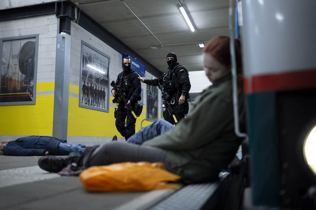Twee gemaskerde GBB’ers kijken naar een vrouw die gewond tegen een tram ligt.