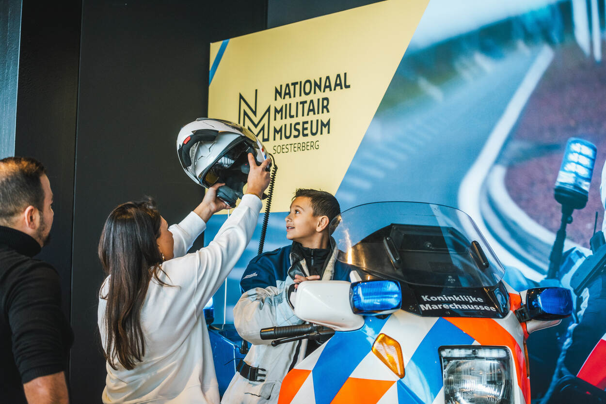 Een jongetje zit op een Marechaussee-motor en krijgt een helm opgezet.