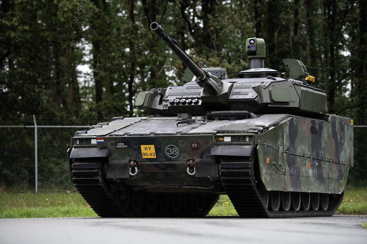 Vernieuwde CV90 op asfalt voor het hek van een kazerne.