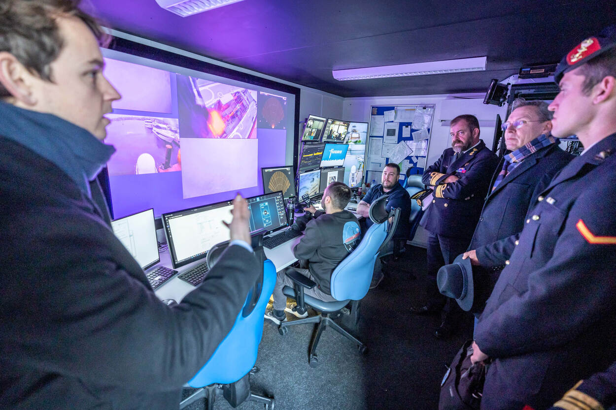 Genodigden kijken mee naar grote schermen met beelden van de zeebodem bij Plymouth.