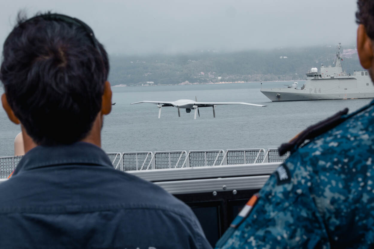 Twee marinemannen op de rug gezien met midden voor hen een vliegende drone.