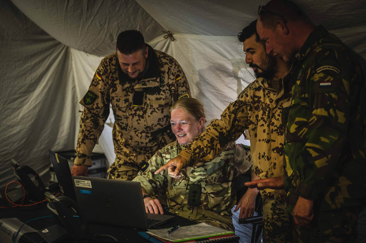 Militairen van verschillende nationaliteiten rondom een laptopscherm.