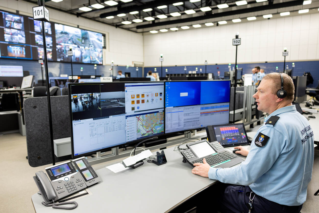 Adjudant Sipke zit achter zijn bureau in de meldkamer. Voor hem grote computerschermen die zijn opgedeeld in kaders, op de achtergrond een muur met daarop led-schermen die verschillende camerabeelden tonen.