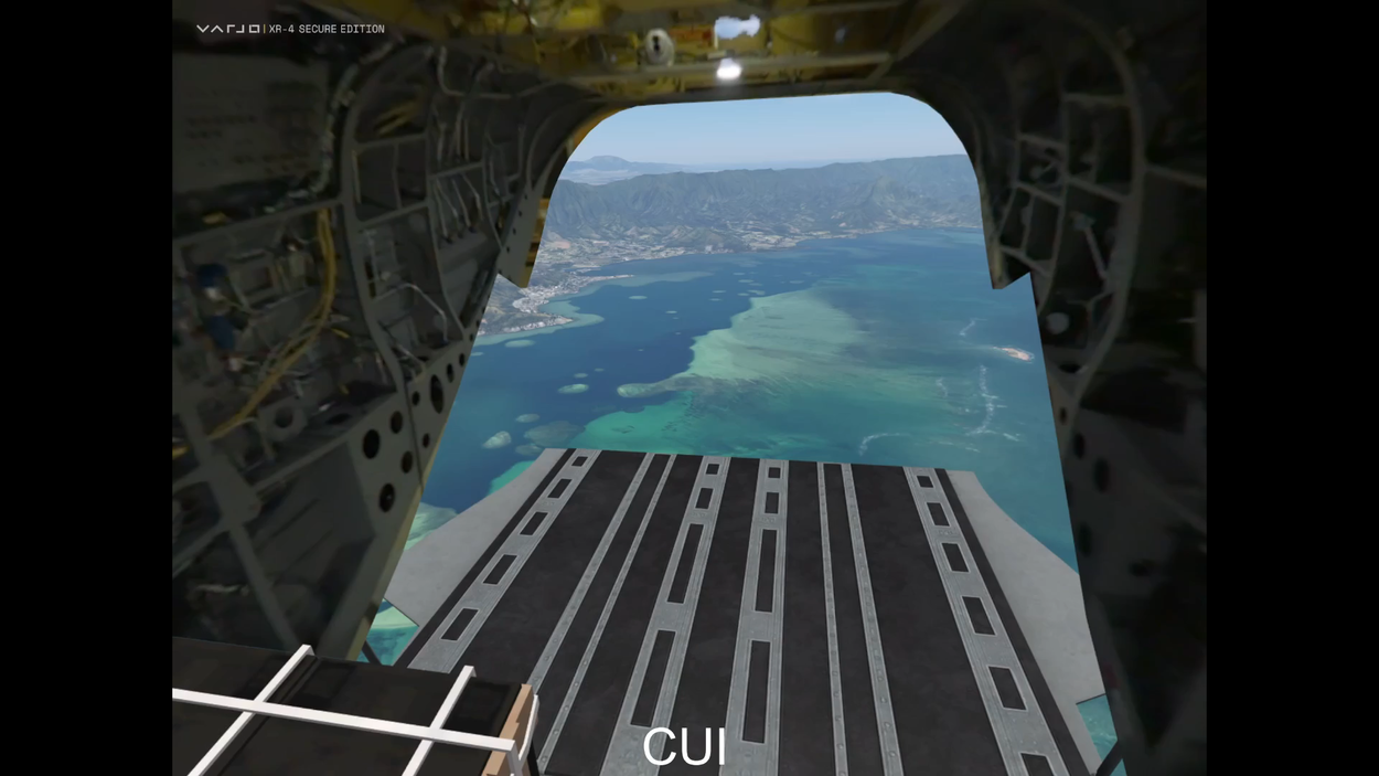 Groot computerscherm toont openstaande laadklep van helikopter die boven zee langs de kust vliegt.