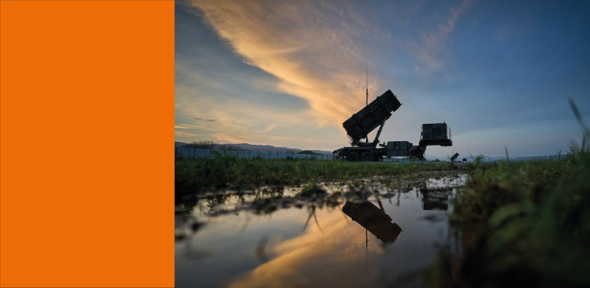 Een luchtafweersysteem in schemer met op de voorgrond een grote plas water waarin het systeem reflecteert.