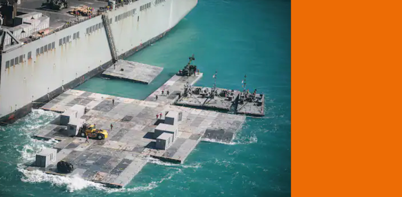 Een drijvende haven van grijze platen met daarop wat loodsen en een bulldozer.