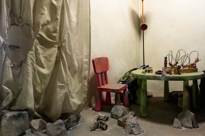 Een kinderstoel en kinderspeelgoed bedekt door stof, te midden van brokstukken.