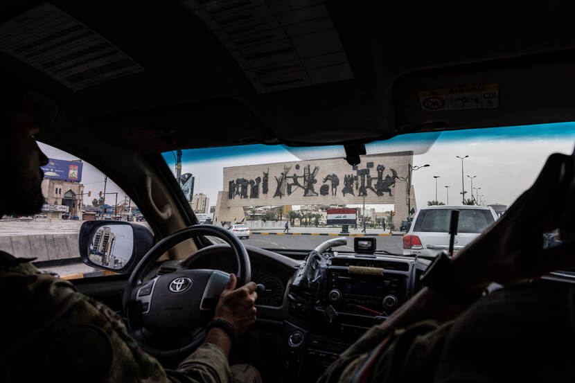 Een militair trekt zijn scherfvest aan in Bagdad. Aan de muur hangt een Nederlandse vlag.