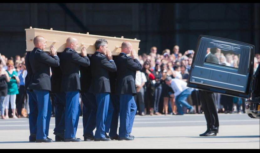 Militairen van de Koninklijke Marechaussee tillen een kist van een MH17-slachtoffer naar een rouwauto