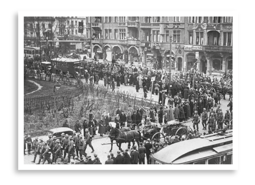 Duitse troepen trekken een stad in Rijnland binnen. Gezien de nazivlaggen aan de gebouwen wordt dat gevierd.