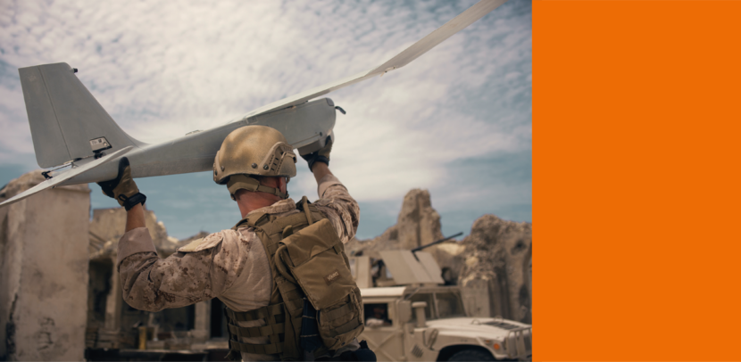 Een militair, gezien van de achterzijde, draagt met beide handen een drone, die hij zometeen in de lucht zal gooien.