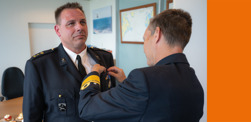 Militair in deftig tenue krijgt ereteken opgespeld door collega-militair.