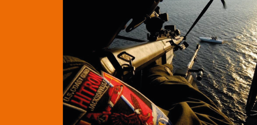 Lid van de kustwacht richt vanuit een helikopter een wapen op een bootje