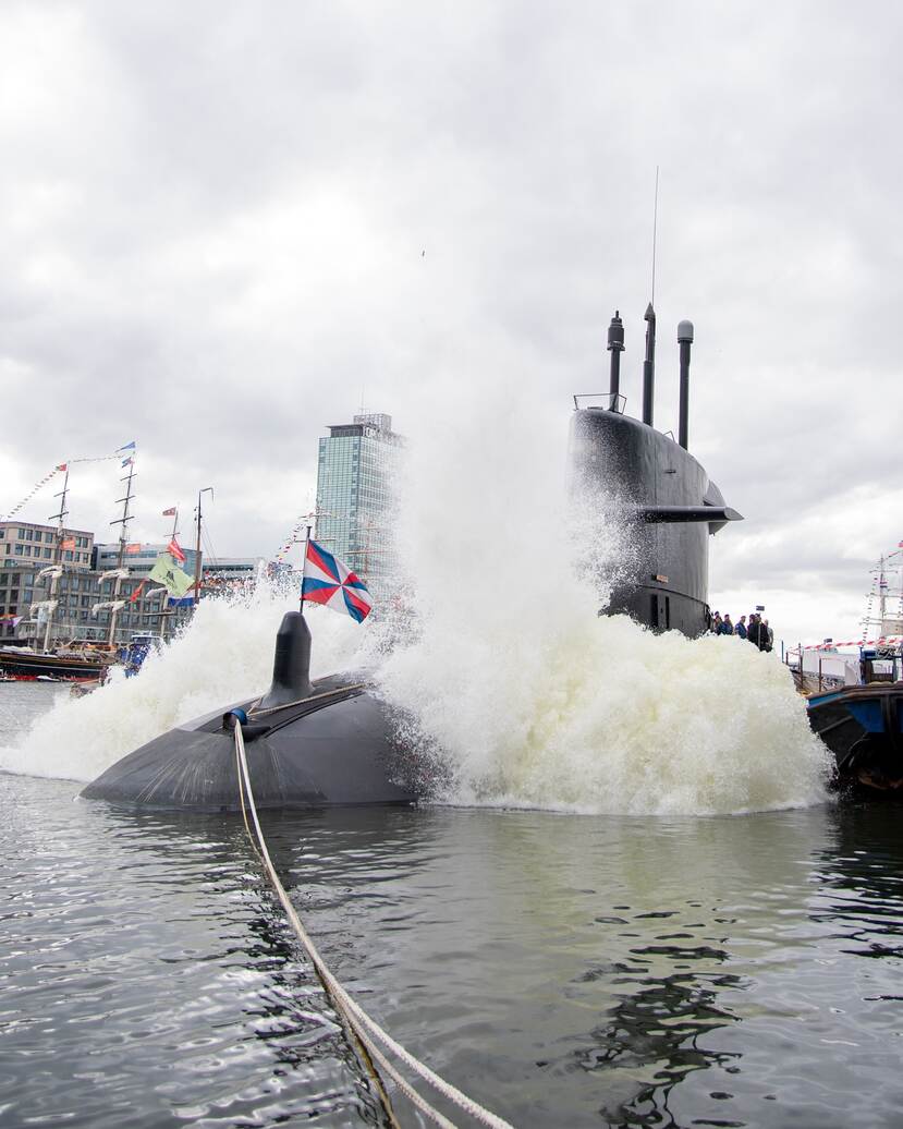 een onderzeeboot veroorzaakt golven aan een havenkade.