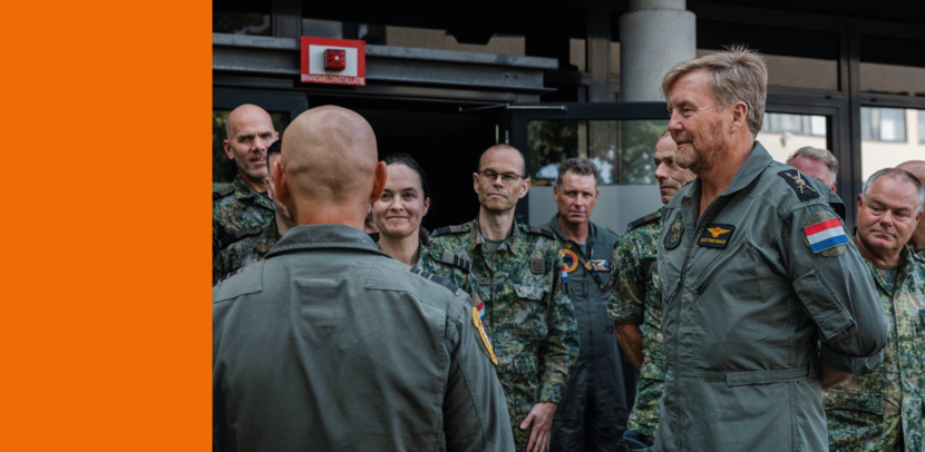 De koning luister in vliegerpak naar andere vliegers.