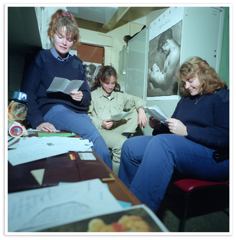 Drie vrouwen zitten gezamenlijk in een kleine ruimte en lezen brieven.