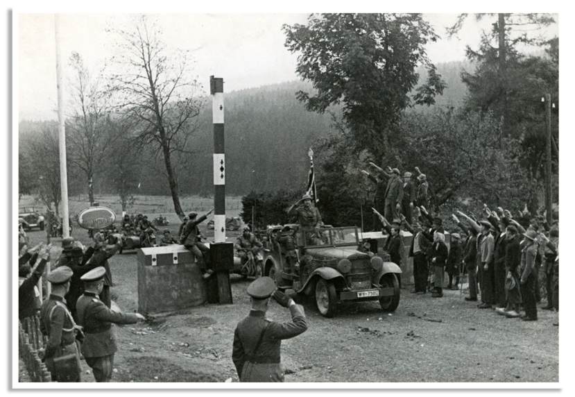 De slagboom bij de grens met Sudetenland staat omhoog als Duitse militairen met motoren en voertuigen er aan voorbij trekken.