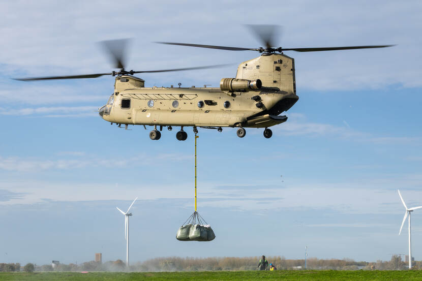 Een Chinook met een lading zakken hangt stil in een weiland.