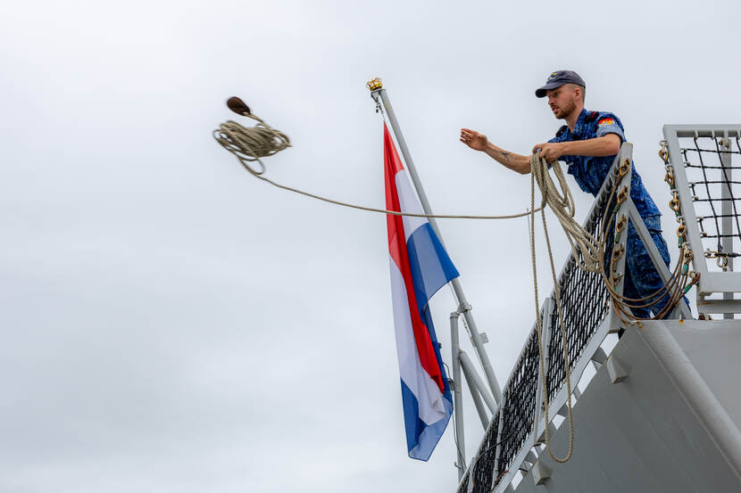 Een opvarende van Zr.Ms. Tromp gooit een tros overboord.